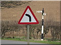 An old metal fingerpost sign with a modern road sign in the foreground