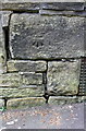 Benchmark on stone over grill in wall on west side of Keighley Road