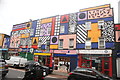 View of Camille Walala street art above The Tyre Shop, Magpie Fun and Games, Magura Romanian shop, a pharmacy and Bar Waqo cafe