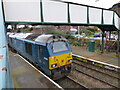 Diesel engine 67001 hauls a train under the footbridge at Helsby station