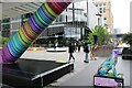 View of Paws for Thought next to the colourful support of Crossrail Place Bridge from Adams Plaza