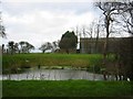 TL2579 : The village pond with farm buildings behind by Chris Stafford