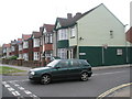 A green car passing a green house in Green Lane